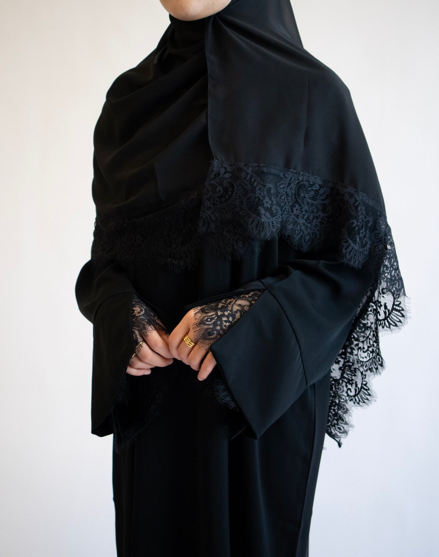Person wearing a black abaya with lace details on a white background