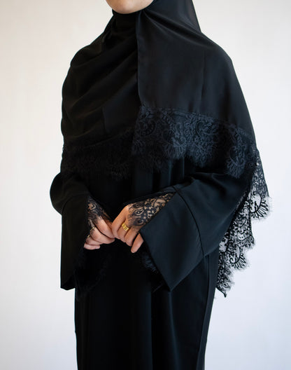 Person wearing a black abaya with lace details on a white background